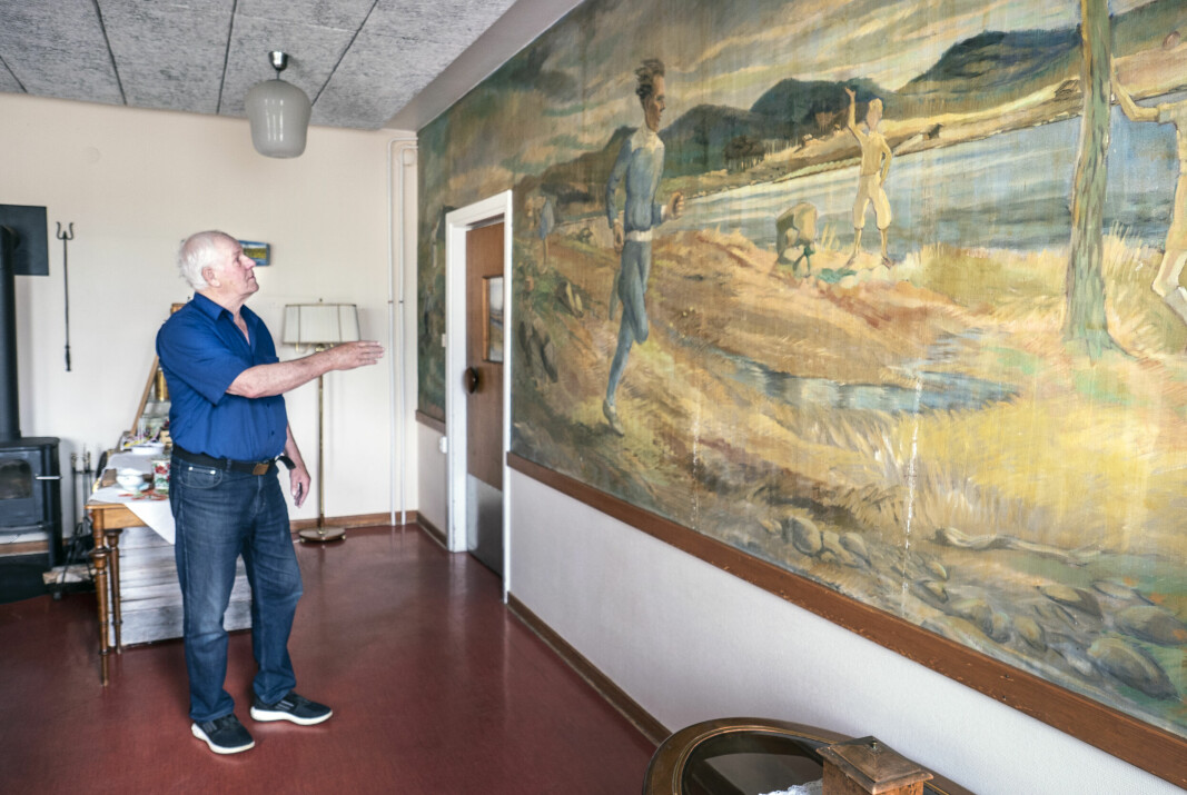 Rolf Adamsson framför den stora målningen på Gunder Hägg. Nu vill han veta vem som har målat tavlan.