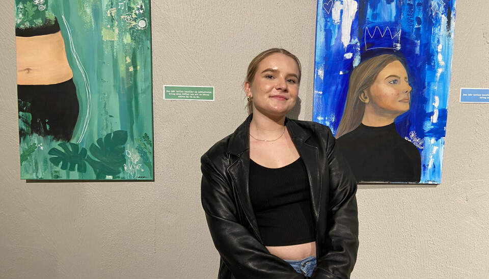 Ebba Löfgren med två av hennes målningar, den med blå bakgrund är ett själv porträtt då hon ville fånga sin sid-profil, en vinkel hon haft svårt för innan.